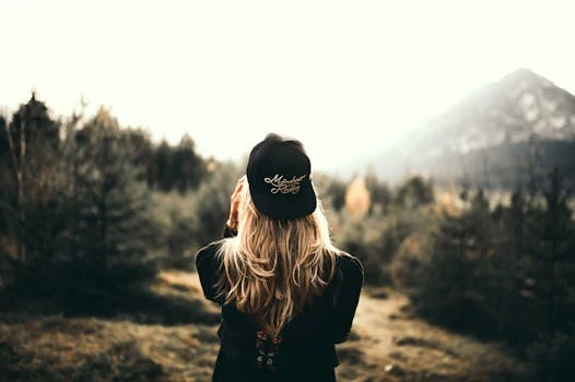 Back view of a woman wearing a cap in front of a mountain landscape